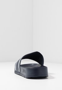 Marinblå slidessandal med öppen tå och bred rem, med vita ränder och texturerad sula, tillverkad av slitstarkt material.