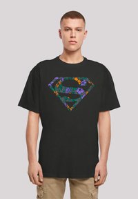 Black cotton t-shirt featuring a colorful floral print of a superhero emblem on the front, with short sleeves and a relaxed fit.
