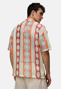 Koszula z krótkim rękawem z siatkowym wzorem w geometryczny wzór w kolorach pomarańczowym, czerwonym, niebieskim i kremowym. Casualowy krój, otwarty kołnierz.