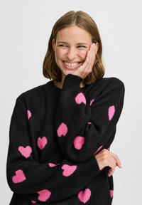 Maglione nero con grandi motivi a forma di cuore rosa, caratterizzato da un colletto rotondo e polsini a costine. Il materiale sembra morbido e strutturato.