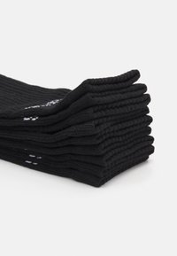 Calzini neri impilati orizzontalmente, realizzati in tessuto a coste. Ogni calzino presenta piccoli accenti bianchi. La texture sembra morbida e elastica.