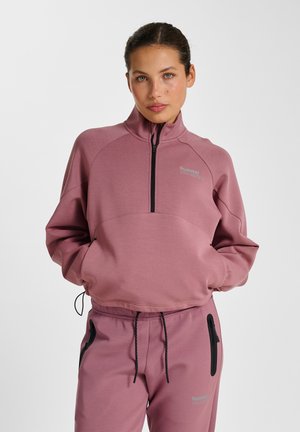 Light pink, long-sleeve pullover with a high collar and half-zip front, featuring a front pocket and black zipper accents. Soft texture.