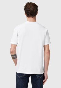 T-shirt bianco a maniche corte, collo rotondo, realizzato in cotone liscio. Indossato con jeans in denim blu scuro. Design semplice, senza motivi o accenti.