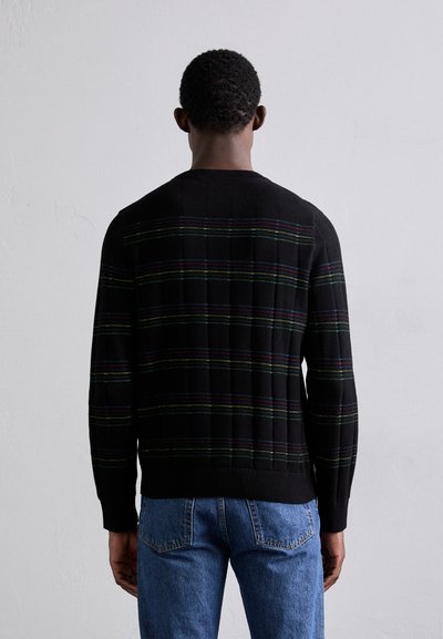 Pull en tricot noir avec des rayures horizontales multicolores, poignets et ourlet côtelés, présentant un motif texturé au dos. Porte avec un jean bleu.