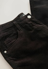Zwarte corduroy broek met een ritssluiting, vijf zakken en contrasterende stiksels, voorzien van een zilveren metalen knoop en label.