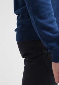 Marinblå stickad tröja med ribbade muddar och nederkant, bärs över svarta byxor och visar en mjuk textur och figurnära passform.