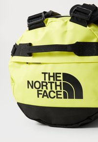 Round bag in bright neon yellow with black accents. Features a prominent logo and sturdy straps, made from textured synthetic material.