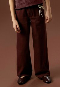 Pantaloni larghi bordeaux in un tessuto morbido, con un cordoncino decorato con perline in vita. Abbinati a scarpe scure semplici.