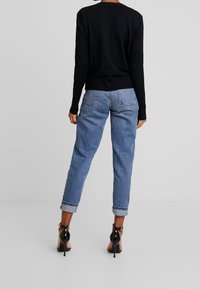 Pull noir à manches longues, texture côtelée, associé à un jean bleu clair avec des ourlets retroussés et des chaussures à talons noirs.