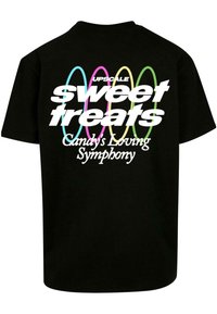 Camiseta de algodón negra con texto blanco y colorido en la parte de atrás: "UPSCALE sweet treats" con "Candy's Loving Symphony" en una fuente más pequeña.