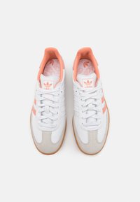 Vita sneakers med ljusorange accenter och grå texturerade överdrag. Funktioner inkluderar snörning, en platt sula och märkets detalj på tungan.