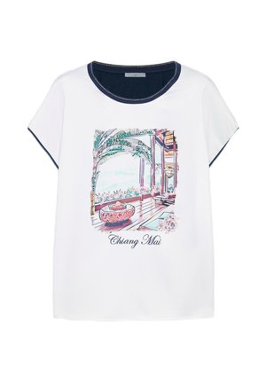 Hvid t-shirt med navyfarvet krave og ærmekanter, der har et farverigt Chiang Mai altanprint med tropiske planter og trægulv.