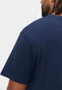 Μπλε βαμβακερό μπλουζάκι με κοντά μανίκια, λαιμόκοψη τύπου crew, λεία υφή και ενισχυμένες ραφές στις ραφές των ώμων.