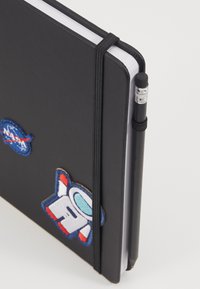 Sort notesbog med et elastisk bånd. Har broderede NASA- og astronaut-patches. Indeholder en blyant, der er sikret i sidelommen.