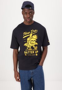 Juodas trumpomis rankovėmis marškinėliai su dideliu geltonu piešiniu, vaizduojančiu beisbolo personažą, su užrašais "New Era" ir "Batter Up" po juo.