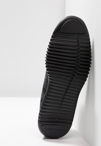 Sole di scarpa sportiva nera in gomma testurizzata, con rilievi orizzontali e iscrizione del marchio. Punta arrotondata e leggera elevazione del tacco.