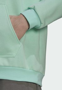 Mintgroene sweatshirt met een kangaroozak, ribbelmanchetten en textiel met structuur. Zichtbare naden bij de zak en de zoom.