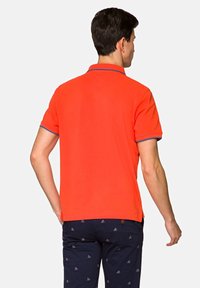 Czerwona koszulka polo z krótkimi rękawami, z kontrastującymi niebieskimi wykończeniami na mankietach i kołnierzyku, wykonana z gładkiego materiału, prezentowana od tyłu.