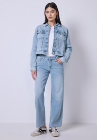 Giacca di jeans azzurro chiaro e jeans a gamba larga, abbinati a una t-shirt bianca. Le sneakers presentano dettagli neri. Texture scolorita sul denim.