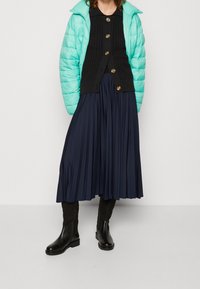 Vadderad mintgrön jacka, svart stickad kardiagan med gulddetaljer, veckad marinblå kjol och svarta ankelstövlar. Texturerade material genomgående.