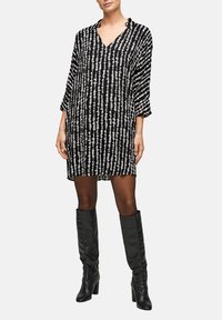 Svartvitt klänning med lös passform, V-ringning och trekvartslång ärm med ett vertikalt randigt mönster. Återigen med knähöga svarta stövlar.