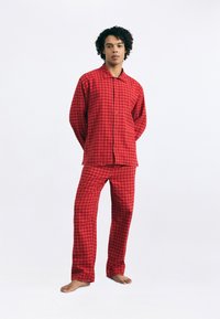 Red checkered pajama set made of soft fabric. Features long sleeves, button-up shirt, and matching pants with an elastic waistband.