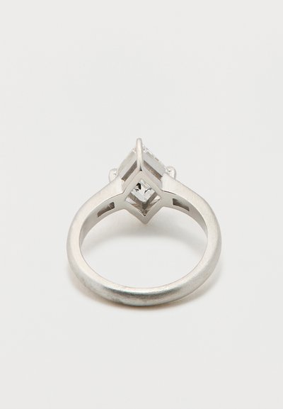 Ezüst gyűrű, keskenyedő szalaggal, a tetején egy kiemelkedő négyzet alakú kővel, amelyet négy kapocs vesz körül, sima felülettel.