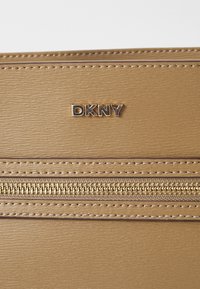 DKNY beige leather wallet with a smooth texture, featuring a gold zipper and embossed logo. Stitched detailing adds structure.