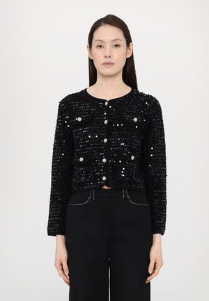 Musthave mustrooni cropped jakk, millel on ümmargune kaelus, ees taskud ja läikivad nööbid. Kombineeritud kõrge vöökohaga mustade pükstega.
