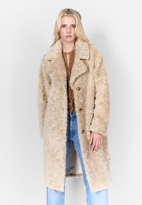 Beige nep-bontjas met een gekartelde kraag, knopen aan de voorkant en een ontspannen pasvorm, met lange mouwen en zijzakken. Geschikt voor casual kleding.