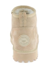 Botín de tobillo de ante beige con un cuello texturizado, suela de goma y un parche circular con el logo en el talón. Cuenta con una resistente tira de agarre acanalada.