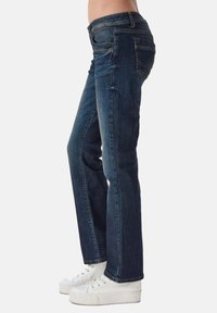 Jeans blu scuro a gamba dritta, con cinque tasche e vita media. Indossati con sneaker bianche.