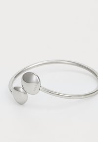 Sølv metallarmbånd med en glatt, avrundet design som har to ovale detaljer. Merket "BOSS" er gravert på en av detaljene.