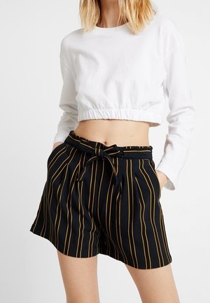 Sweatshirt blanc court avec un ourlet resserré, associé à un short noir taille haute arborant des rayures verticales jaunes et un détail de taille nouée.