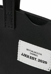 Czarna skórzana torba tote z szytymi uchwytami, z białą etykietą z napisem "BĄDŹ ZABAWNY, ODWAŻNY I ŚMIAŁY" oraz "JJXX ZAŁ. 2020.".