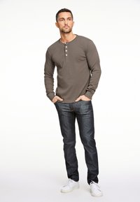 Olijfgroene henley-shirt met lange mouwen en drie knopen, gecombineerd met donkerblauwe spijkerbroek en witte sneakers. Soepele textuur.