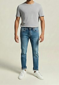Lichtgrijze t-shirt met korte mouwen, in combinatie met vervaagde blauwe denim jeans en witte sneakers. De jeans zijn taps toelopend met een opgerolde zoom.
