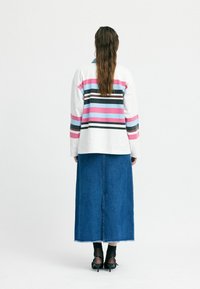 Langärmliges, kragenloses Oberteil mit horizontalen Streifen in Pink, Blau und Schwarz. Kombiniert mit einem langen Jeansrock und schwarzen High Heels.