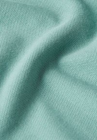 Tissu bleu clair texturé avec un motif fin tissé en forme de grille et des plis doux créant des ombres délicates.