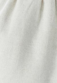 Naravni laneni material v barvi slonokoščene bele, z grobo teksturo in subtilnimi odtenki, ki prikazuje mehko, zloženo teksturo.