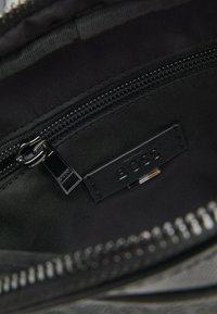 Black fabric interior of a bag featuring a zipper closure and a label with "BOSS" branding. Smooth texture with subtle sheen.