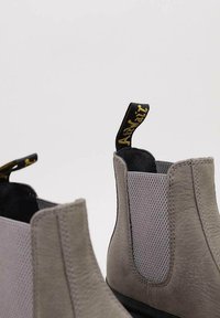 Harmaat Chelsea-bootit, jotka on valmistettu nahasta ja verkkokankaasta. Varustettu teksturoidulla pinnalla, joustavilla sivupaneeleilla ja vetotapilla, jossa on kultateksti.