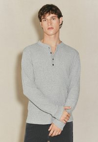 Grå langærmet henley-skjorte med et tekstureret strikmateriale, der har en delvis knaplukning og tapered manchetter for et tætsiddende look.