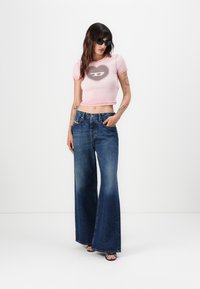 Cropped pink T-shirt with a heart logo, paired with wide-leg dark blue jeans. Model wearing black sunglasses. Smooth fabric and denim texture.