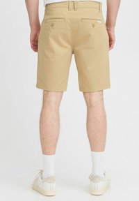 Shorts en khaki fabriqués en coton, avec une coupe classique. La vue de dos montre deux poches à boutons et une texture lisse. Portés avec des baskets légères.