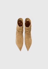 Stivali ankle in suede beige con punta affusolata e materiale arricciato attorno alla caviglia, con una fodera interna liscia.