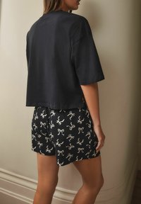 Black cropped t-shirt with short sleeves paired with black shorts featuring a white bow pattern. Soft cotton material visible.