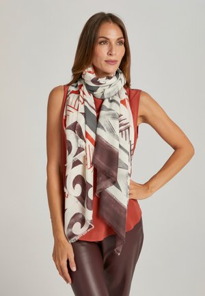 Grand foulard rectangulaire blanc avec des motifs abstraits rouges et gris. Bords effilochés, tissu léger, drapé élégamment autour du cou.