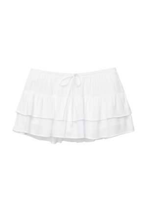 Jupe blanche à volants en trois niveaux, taille élastique et cordon de serrage. Fabriquée en tissu léger et texturé.