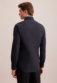 Camicia a manica lunga di colore blu navy scuro realizzata in tessuto testurizzato, dotata di colletto classico e polsini con bottone, con un orlo curvo sul retro.